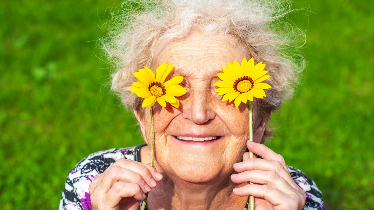 Äldre glad kvinna håller blommor framför ögonen