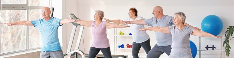 Ett gäng äldre män och kvinnor stretchar på varsin yogamatta.