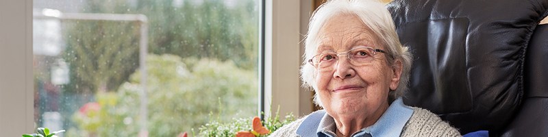 En äldre dam sitter i en fåtölj vid ett fönster
